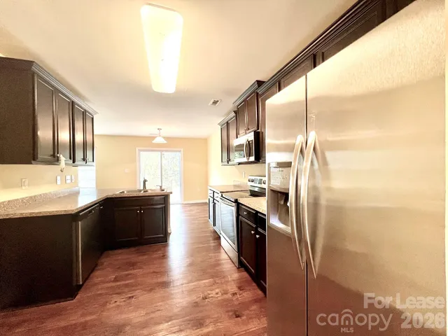 a large kitchen with stainless steel appliances kitchen island granite countertop a refrigerator and a sink