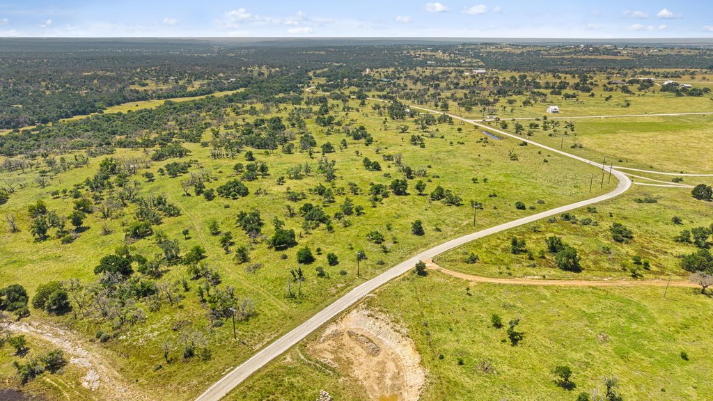 Vast green acreage featuring a winding road, dotted with trees under an open sky.
