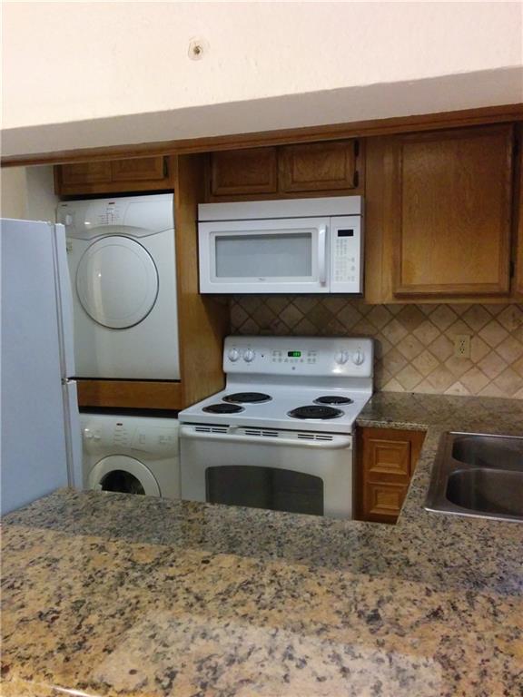 3506 Speedway, Unit 106 Austin, TX 78705 - Photo 8 of 9 Kitchen featuring white appliances, wood finish cabinets, stacked washer and dryer, tasteful backsplash, and dark stone countertops