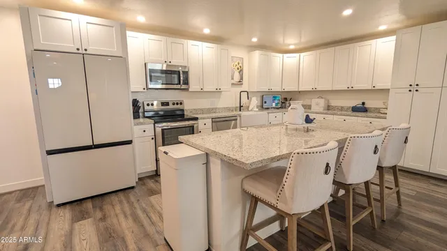 a kitchen with stainless steel appliances a stove a sink a refrigerator white cabinets and wooden floor