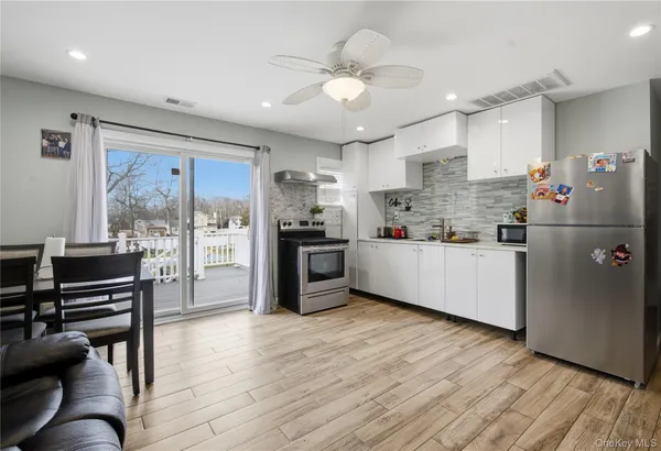 a kitchen with stainless steel appliances kitchen island granite countertop a refrigerator a stove a sink a dining table and chairs with wooden floor