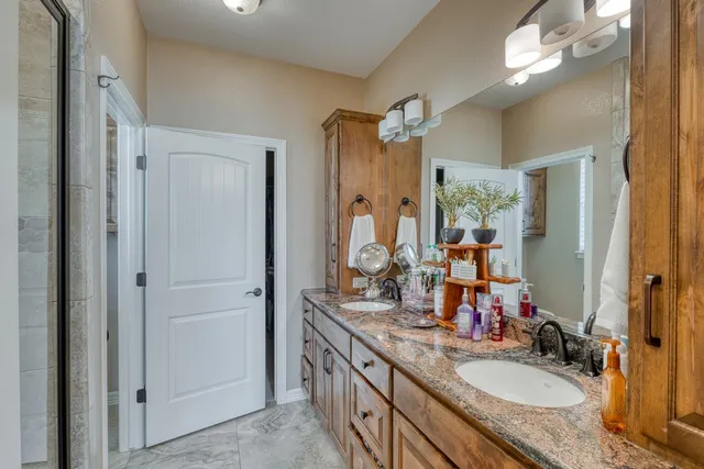 a bathroom with a granite countertop double vanity sink a mirror and a shower