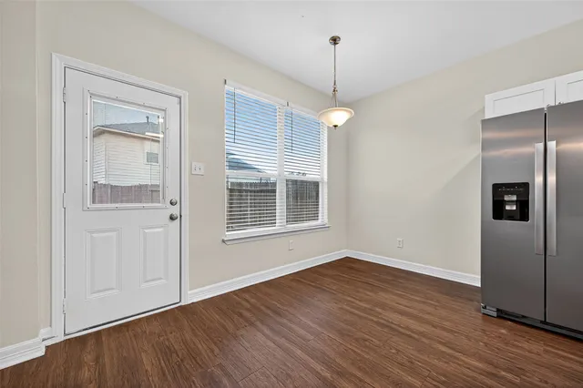 a view of an empty room with wooden floor fridge and a window