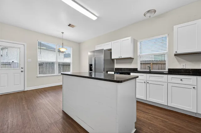 a kitchen with stainless steel appliances white cabinets a sink a stove a refrigerator and wooden floors