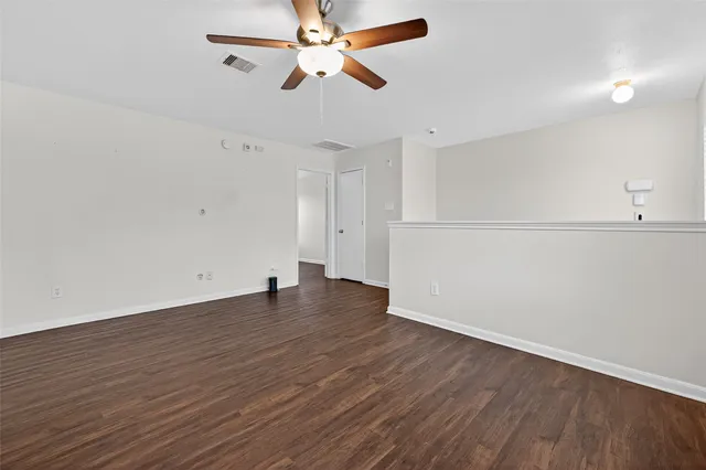 an empty room with wooden floor ceiling fan and windows