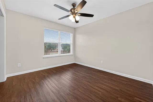 an empty room with wooden floor ceiling fan and windows