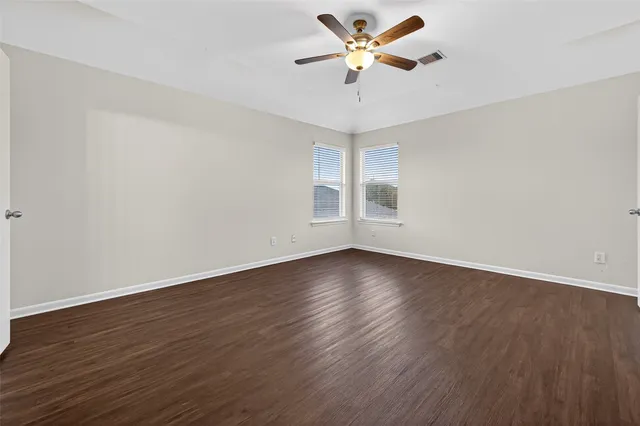 an empty room with wooden floor fan and windows