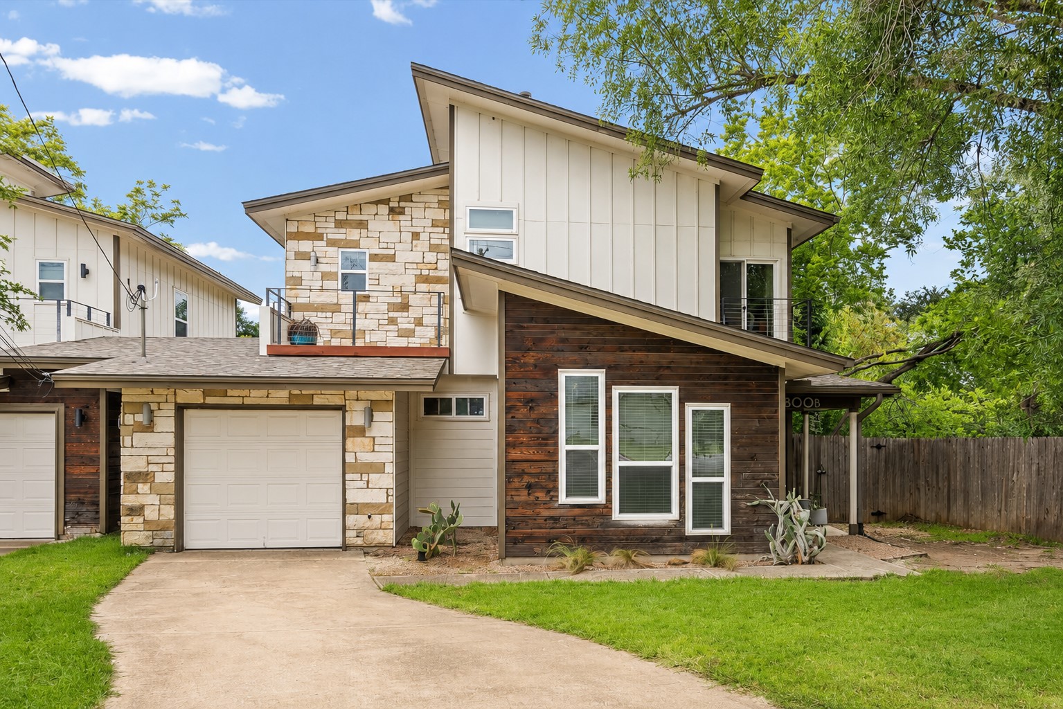 1800 Webberville Road, Unit B Austin, TX 78721 - Photo 2 of 30 Contemporary exterior featuring a stone and wood panel facade, an attached garage, a second-story balcony with metal railings, and multiple large windows