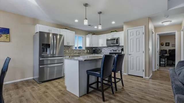 a kitchen with stainless steel appliances granite countertop a refrigerator a stove a microwave oven a sink with island and chairs with wooden floor