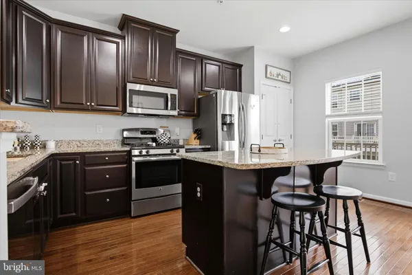a kitchen with stainless steel appliances granite countertop wooden cabinets a refrigerator a stove a sink and dishwasher with wooden floor