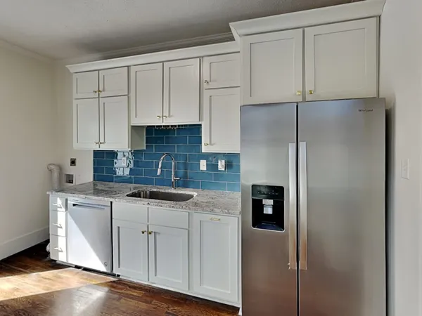 a kitchen with stainless steel appliances granite countertop a refrigerator a sink and white cabinets