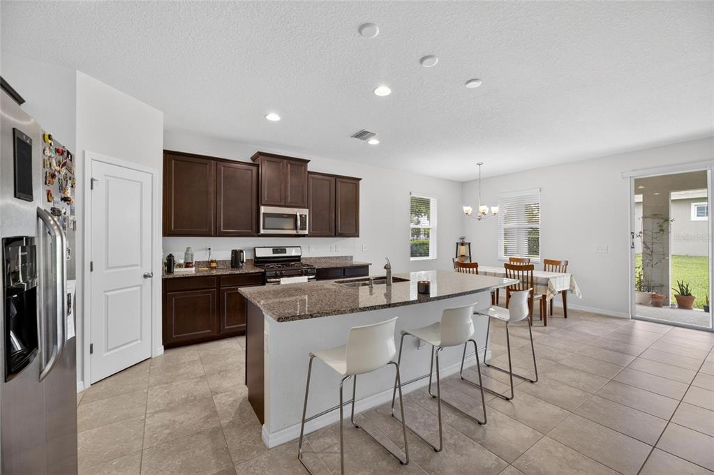 6309 Shadowlake Drive Apollo Beach, FL 33572 - Photo 10 of 64 a kitchen with stainless steel appliances granite countertop a stove top oven a sink a refrigerator and a dining table with white cabinets