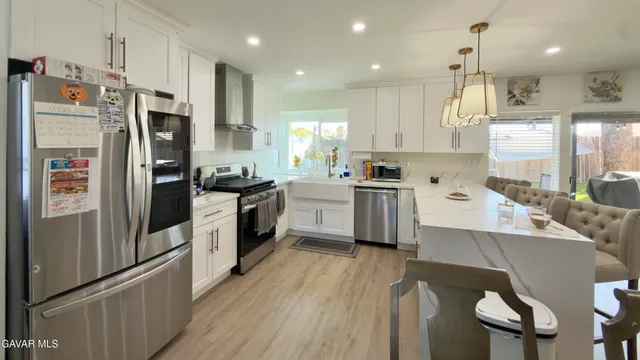 a kitchen with stainless steel appliances a refrigerator a sink dishwasher a stove and white cabinets with wooden floor