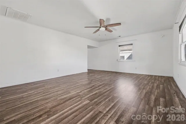 an empty room with wooden floor fan and windows