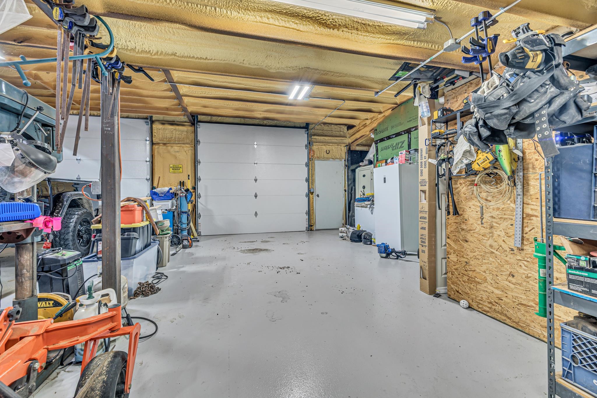 350 Hamilton Road Springville, TN 38256 - Photo 28 of 40 Spacious garage interior featuring two white paneled garage doors, exposed wood beam ceiling, and fluorescent overhead lighting