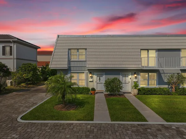 a view of a white house next to a yard with big trees