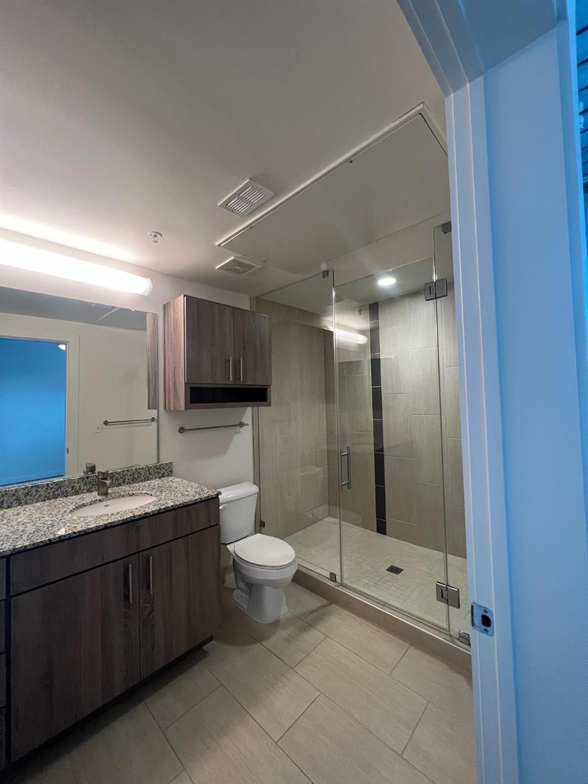 3550 Main Street, Unit 7126 Houston, TX 77002 - Photo 7 of 49 This modern bathroom features a spacious glass-enclosed shower, granite countertop with a single sink, and sleek wood cabinetry. The neutral tile flooring and contemporary lighting create a clean and inviting space.