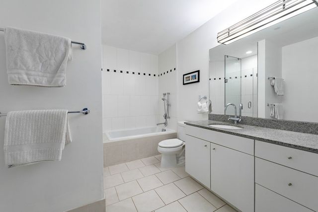 a bathroom with a granite countertop sink a toilet a mirror a vanity and bathtub