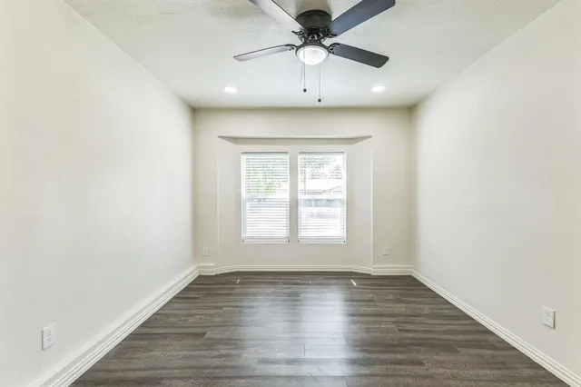 an empty room with wooden floor chandelier fan and windows