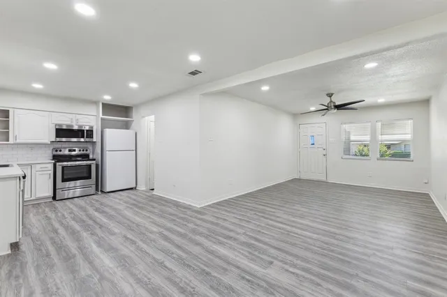 an empty room with wooden floor kitchen view and windows