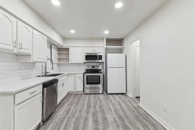 a kitchen with stainless steel appliances granite countertop a refrigerator a sink dishwasher a stove and white cabinets with wooden floor