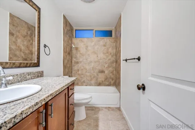 a bathroom with a granite countertop sink a toilet a mirror a vanity and bathtub