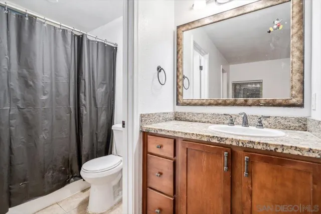 a bathroom with a granite countertop sink a toilet a mirror and shower