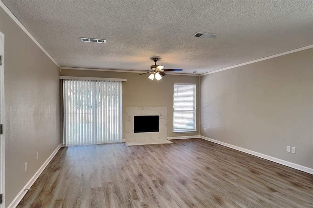 7309 Indiana Avenue Fort Worth, TX 76137 - Photo 3 of 18 Unfurnished living room featuring a high end fireplace, light wood-style floors, a textured ceiling, a ceiling fan, and ornamental molding