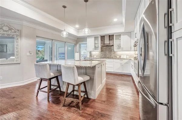 a kitchen with stainless steel appliances granite countertop a refrigerator a sink dishwasher a stove and white cabinets with wooden floor