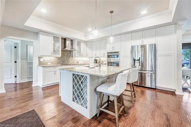 a kitchen with stainless steel appliances granite countertop a refrigerator a sink dishwasher a stove and white cabinets with wooden floor