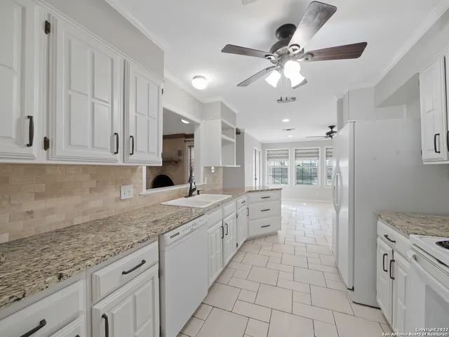 a large white kitchen with granite countertop a sink dishwasher a stove and a refrigerator with wooden cabinets