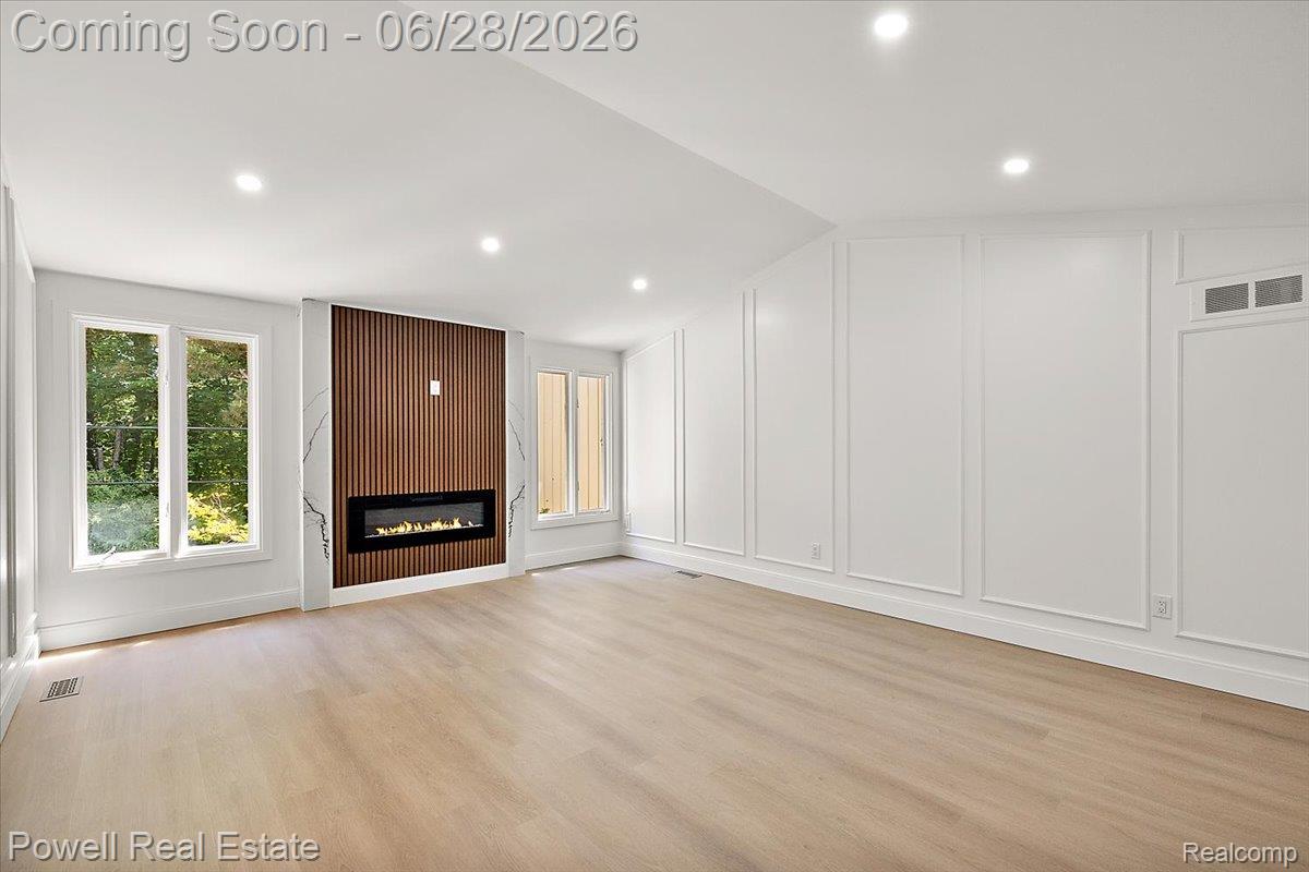 1447 Ravineview Court, Unit C12 Bloomfield Hills, MI 48304 - Photo 30 of 49 Contemporary living space featuring a linear electric fireplace with a wood-slat and marble-look surround, light wood-finish flooring, recessed lighting, white wall paneling, and multiple windows