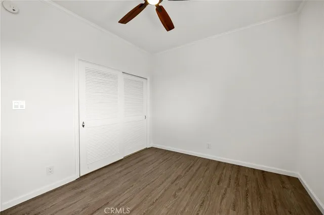 a view of an empty room with wooden floor and a ceiling fan