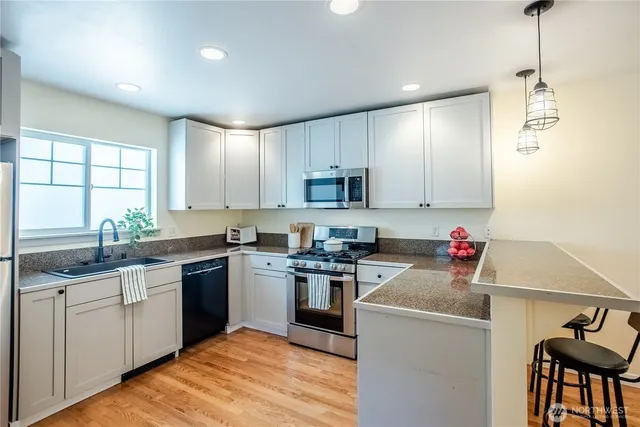 a kitchen with granite countertop a sink cabinets stainless steel appliances and a window