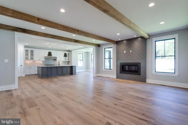 a view of an empty room with wooden floor and kitchen view