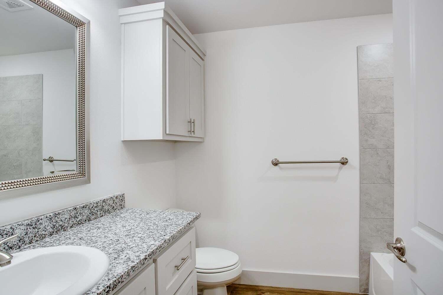 811 North 4th Street Wolfforth, TX 79382 - Photo 16 of 18 a bathroom with a granite countertop sink toilet a mirror and shower