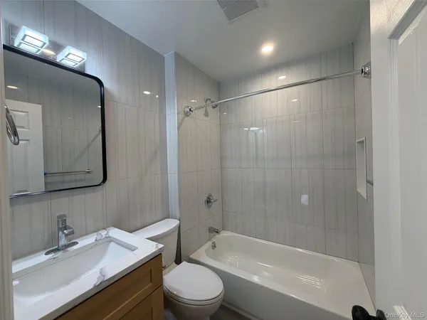 a bathroom with a bathtub shower sink vanity mirror and toilet
