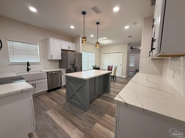 a large kitchen with a large counter top a sink stainless steel appliances and cabinets
