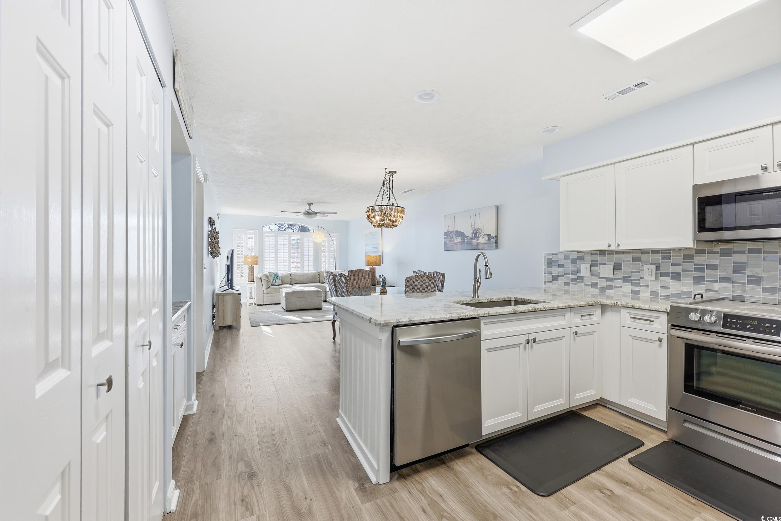 448 Pinehurst Lane, Unit 16F Pawleys Island, SC 29585 - Photo 31 of 31 Kitchen featuring appliances with stainless steel finishes, white cabinets, backsplash, light stone countertops, and open floor plan