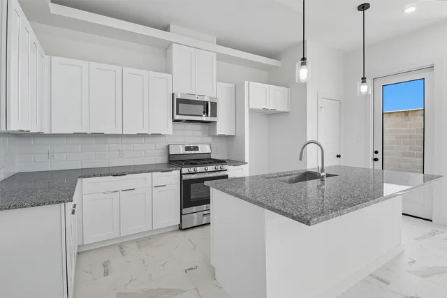 a kitchen with stainless steel appliances granite countertop a sink a stove a refrigerator and white cabinets