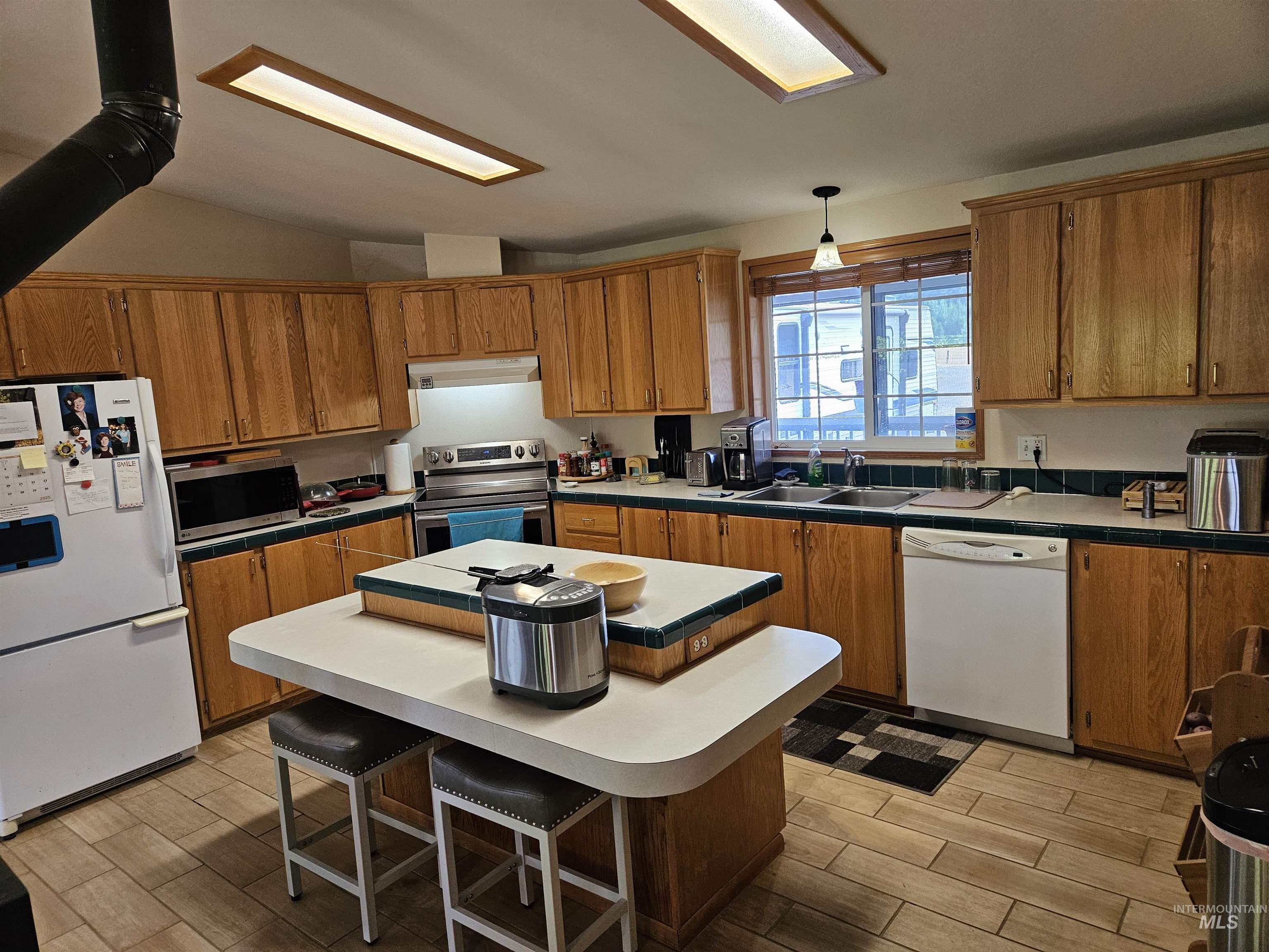 232 Lackey Road Weippe, ID 83553 - Photo 3 of 33 Kitchen with stainless steel appliances, brown cabinetry, wood finish floors, tile counters, and a center island