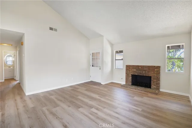 an empty room with wooden floor fireplace and windows
