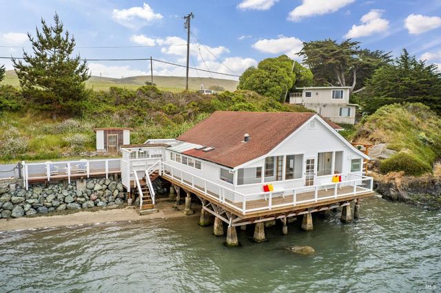 a white house with a large pool and lawn chairs under an umbrella