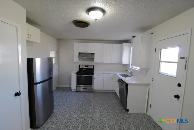 a kitchen with stainless steel appliances a refrigerator a sink a stove a table and chairs