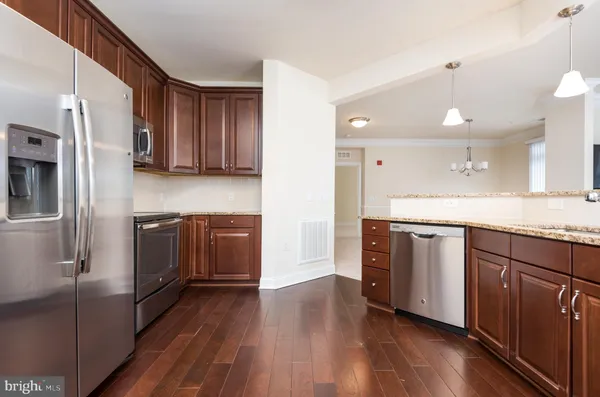 a kitchen with stainless steel appliances granite countertop a refrigerator a sink dishwasher a stove and white countertops with wooden floor