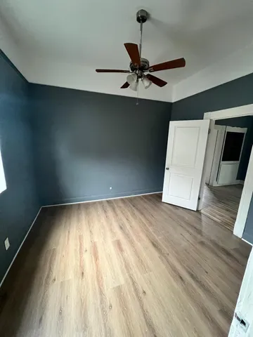 a view of an empty room with wooden floor and a ceiling fan