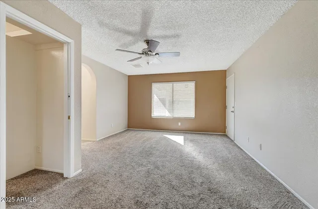 an empty room with chandelier fan and windows