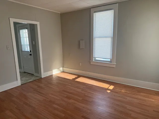 a view of an empty room with wooden floor and a window