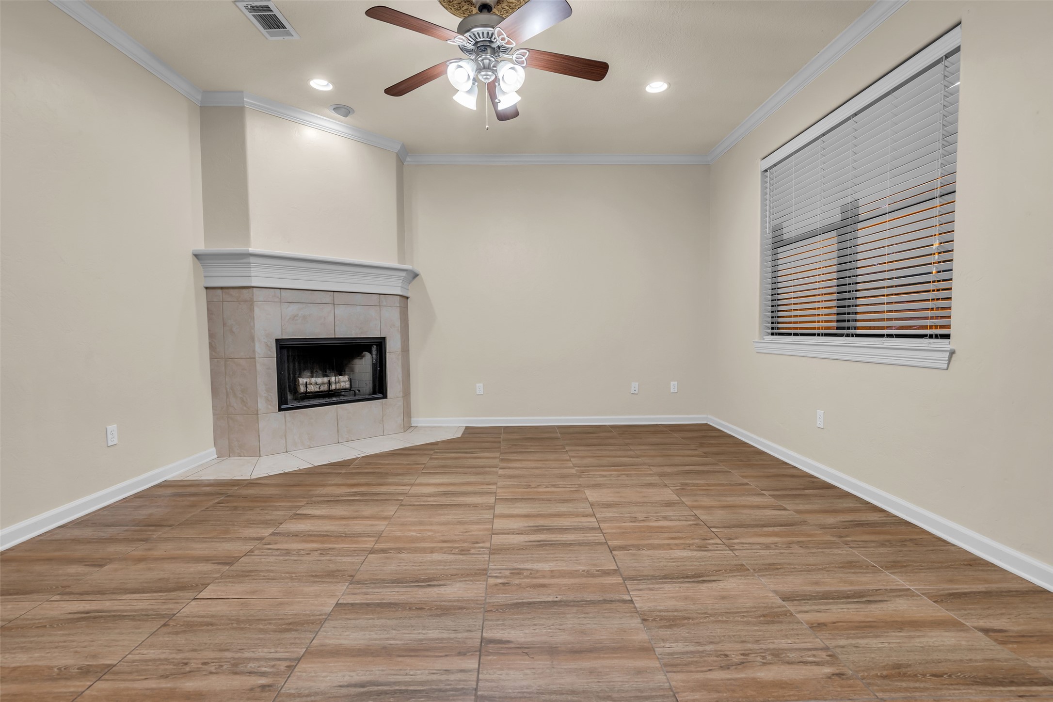 1898 Longmire Road, Unit 5 Conroe, TX 77304 - Photo 13 of 48 This room features a cozy corner fireplace with a tiled surround, neutral-colored walls, and wood-look tile flooring. A ceiling fan and large window with blinds enhance the space, providing comfort and natural light.