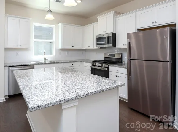 a kitchen with granite countertop a refrigerator a sink a stove a microwave and island